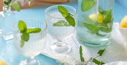 Two glasses with water and mint and a jug of water and mint on blue table