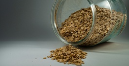 A glass jar of oats spilling onto a white counter