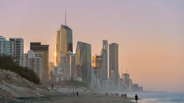 An eroded beach with skyscrapers in the background on the coastal fringe.