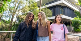 Three female students smiling in front of learning centre