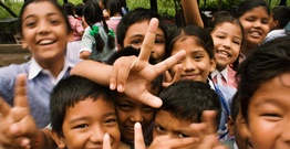 A group of young children crowding camera and holding hands up