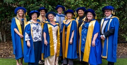 Graduates standing in a group in graduation robes smiling at camera