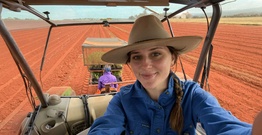 Girl in a hat smiling at camera in tractor with red dirt behind