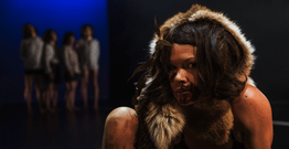 Woman in tribal costume covered in dirt with blurred people in background