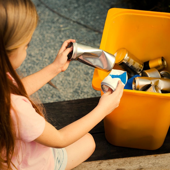 Young girl recycling cans into bin