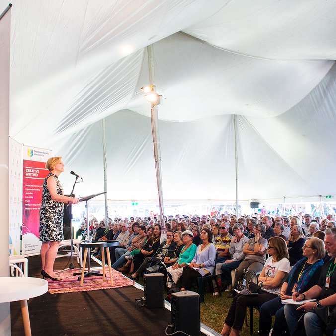 A woman addresses a large group of people under a marquee