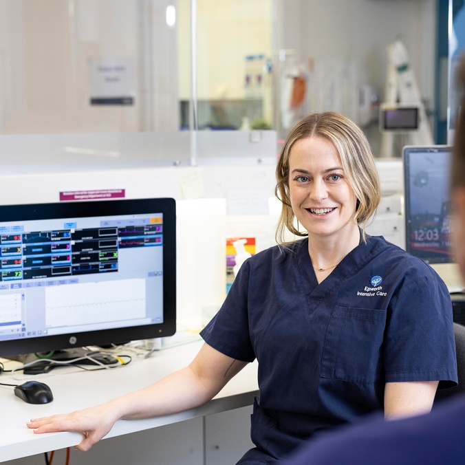 A woman in scrubs talks to a colleague in a hospital setting