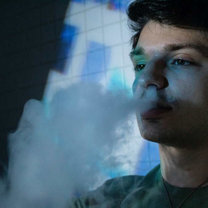 A young man blowing smoke from an e-cigarette
