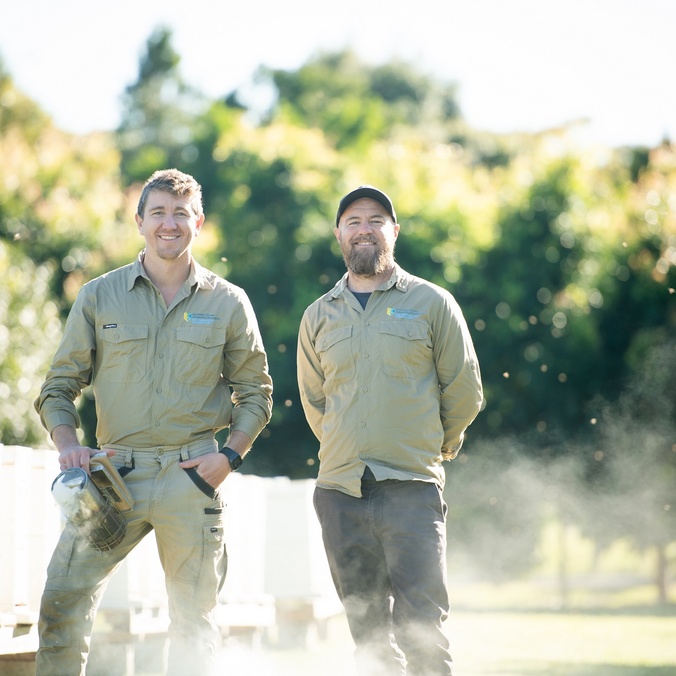 Two men in a field with bee hives in the background