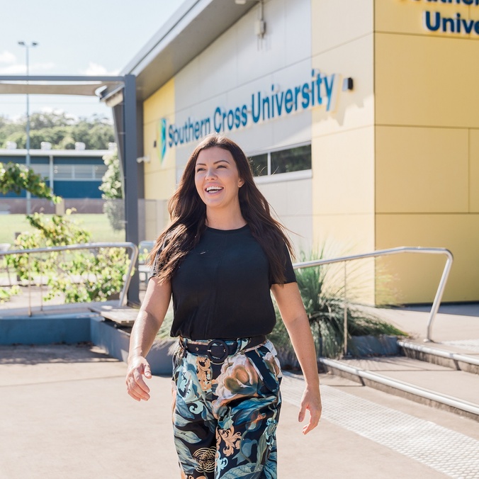 A woman walking away from a yellow fronted building with Southern Cross University logo