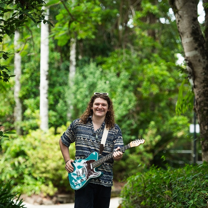 A man with a guitar in a green leafy setting