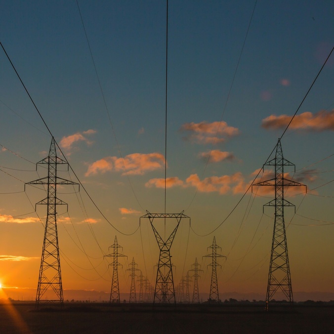 A series of power lines with a setting sun in the background