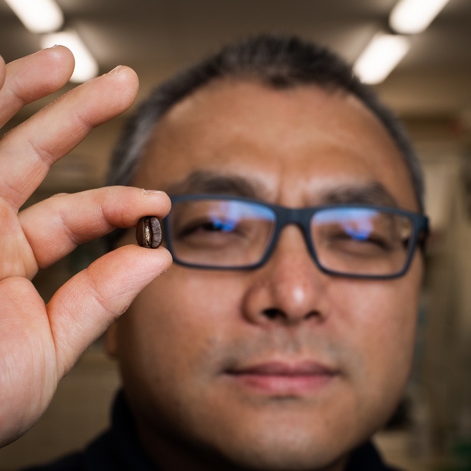 A man holding a coffee bean in front of the camera