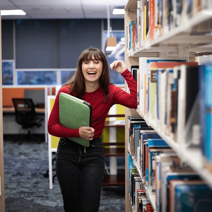 Student in Library surrounded by books on shelf
