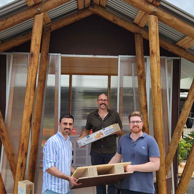 3 men outside a house, holding building materials