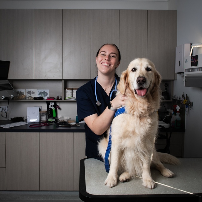 A woman in clinical scrubs with a Golden Retriever looking at the camera