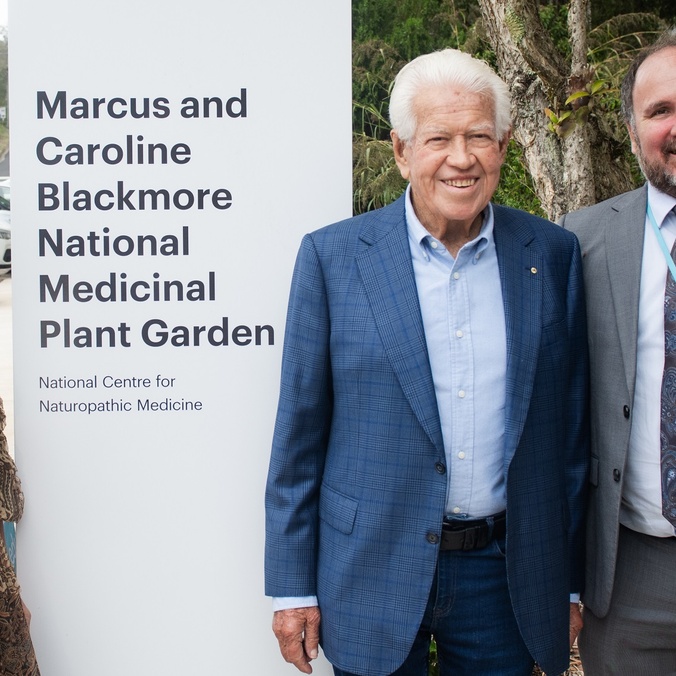 Two men and a woman in front of a sign that says Marcus and Caroline Blackmore Medicinal Plant Garden