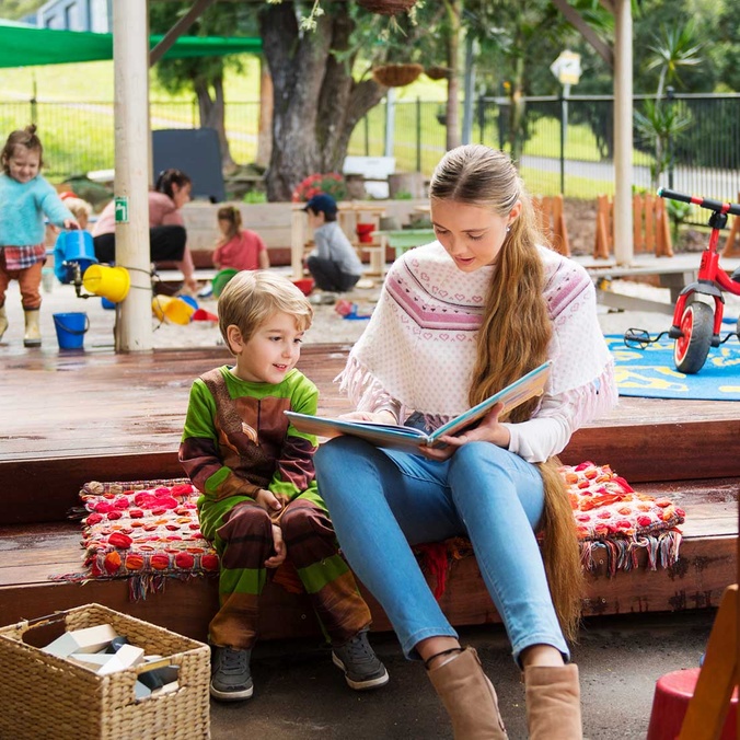 Early Childhood teacher reading with pupil in playground