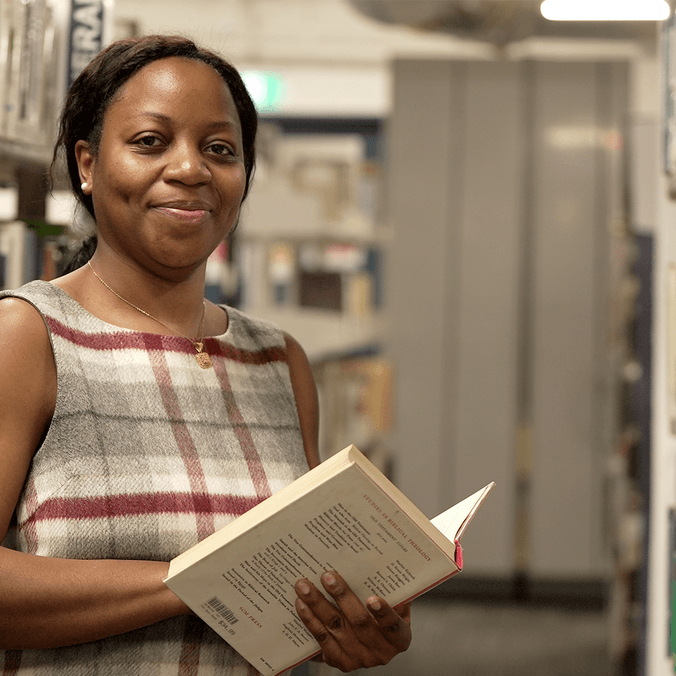 Professor Ebi Cocodia holding open book in library