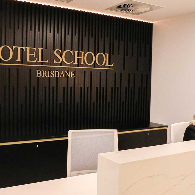 Woman sitting at reception desk with The Hotel School Brisbane sign in background