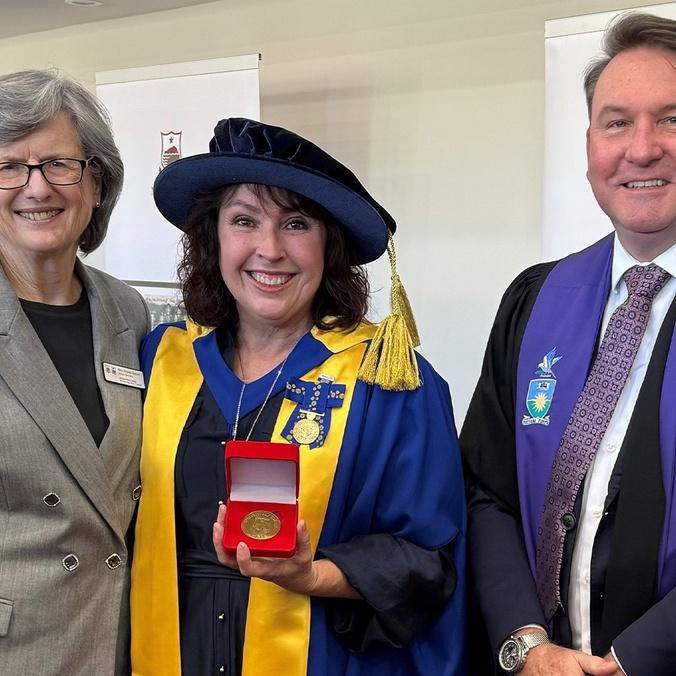 Women in academic dress with medal standing between woman and man