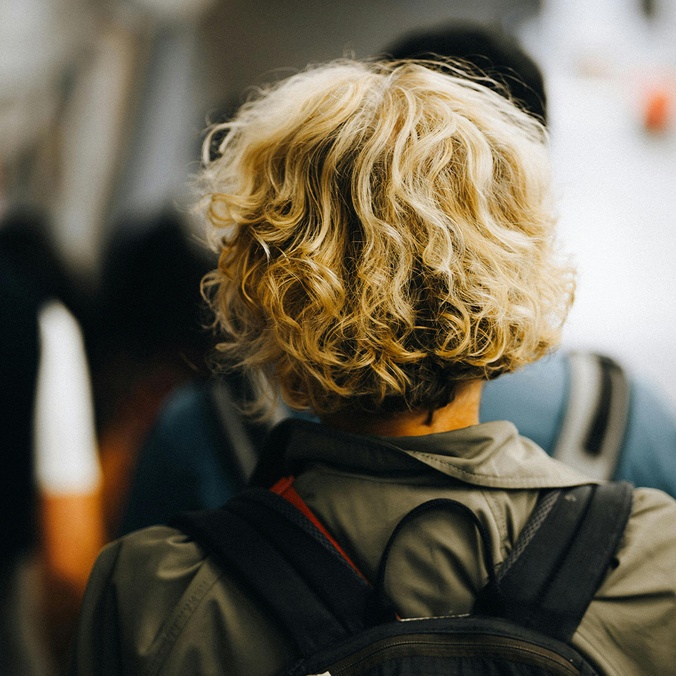Back of head of someone with curly blonde hair wearing a backpack