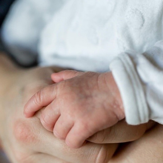 Newborn baby's hand resting on adult hand