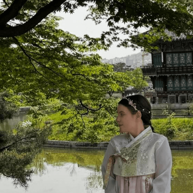 Student in traditional Korean attire in front of river and temple