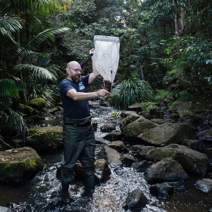 Man standing in a rocky stream holding a large net