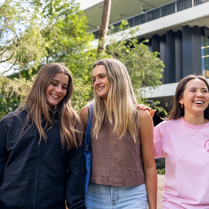 Three female students smiling in front of learning centre