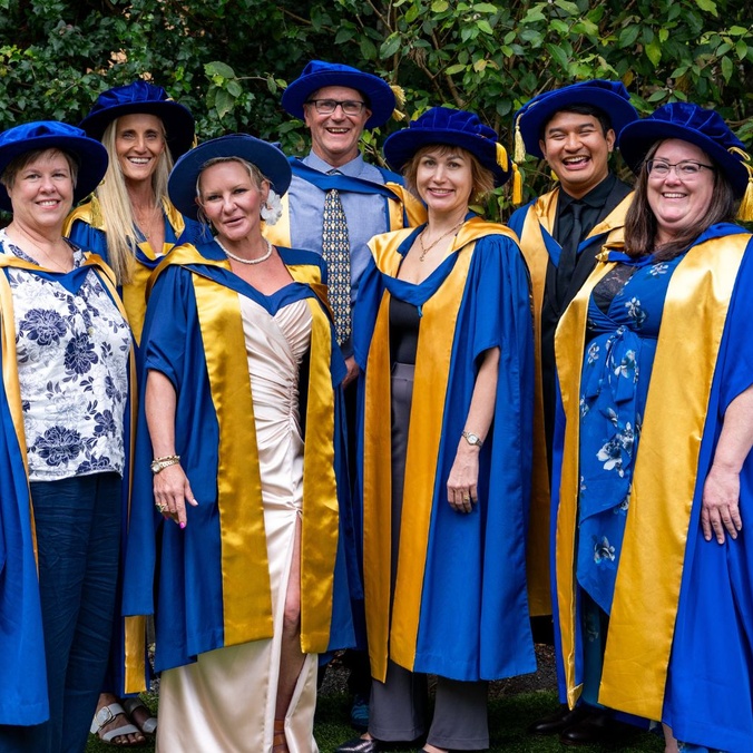 Graduates standing in a group in graduation robes smiling at camera