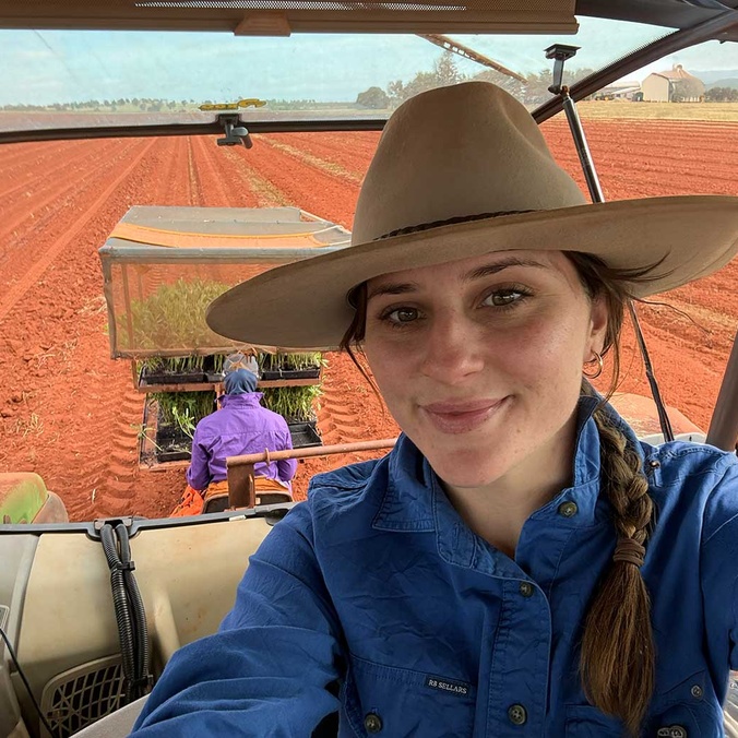 Girl in a hat smiling at camera in tractor with red dirt behind