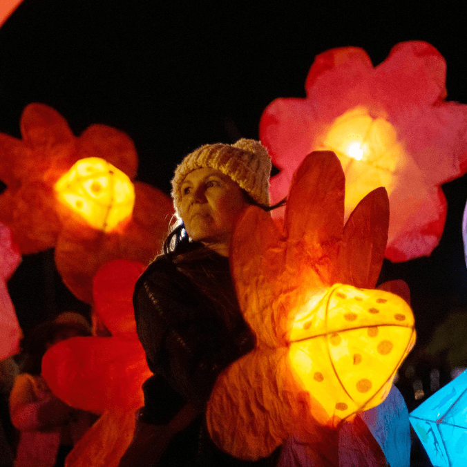 Woman in beanie holding lantern while other flower lanterns float around her