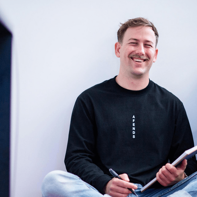 Nathan smiling sitting cross-legged with notebook and pen