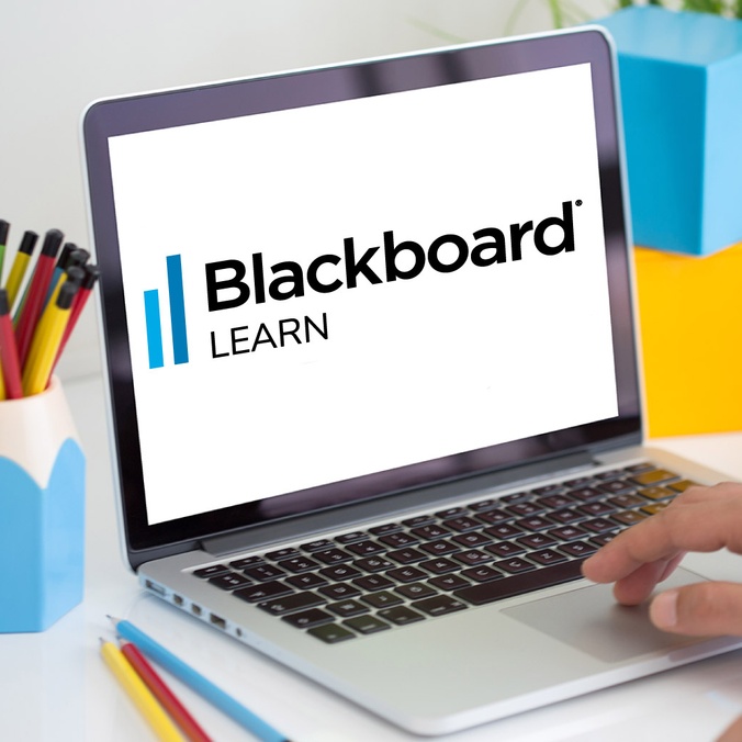 Blackboard Learn logo on a laptop screen sitting on a desk with office supplies surrounding it while a hand types on the keyboard