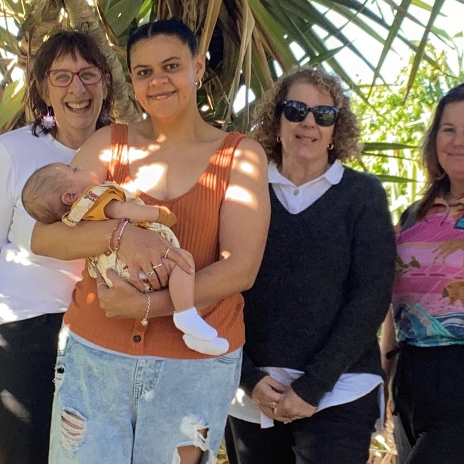 A group of women in front of a pandanus tree, with one of them holding a baby