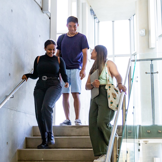 3 international students are walking down some stairs, talking and laughing at the Southern Cross University Gold Coast Campus