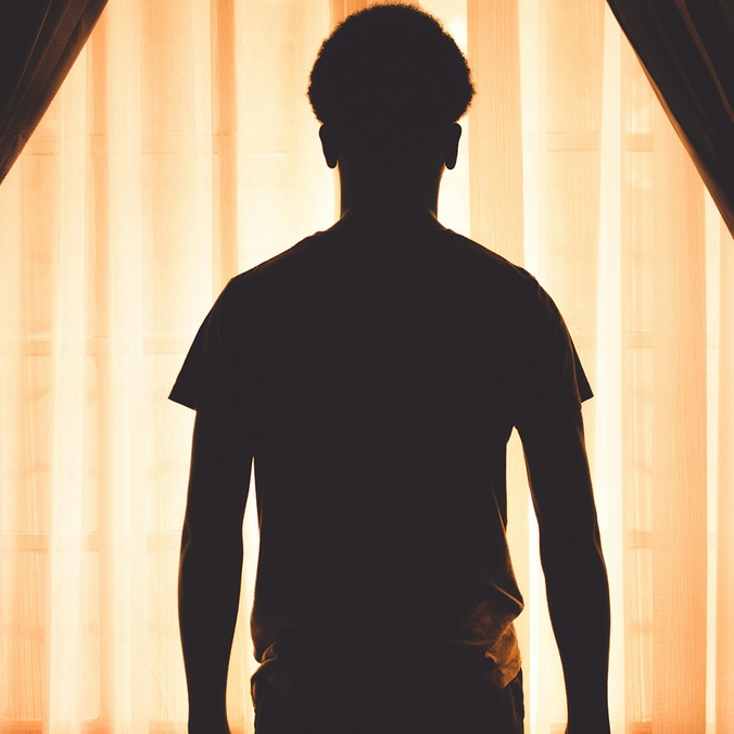 Silhouette of a boy standing against curtains in a dark room