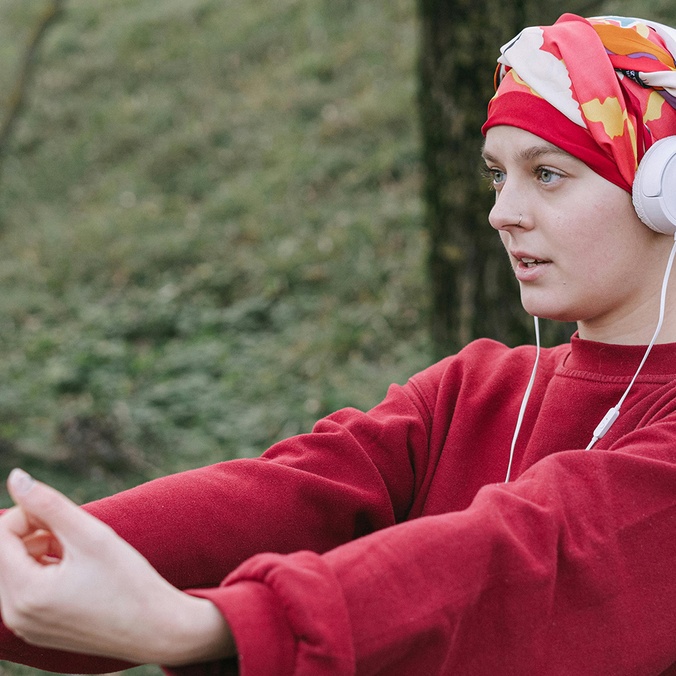 Woman recovering from cancer treatment wearing headphones and doing exercises