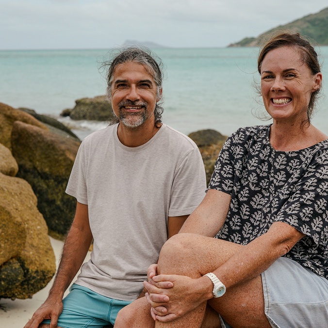 A man and woman sitting on rocks with the ocean and an island in the background