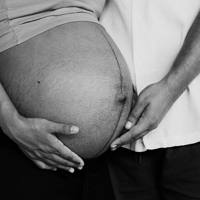 A black and white image of the belly of a pregnant women with male partner touching her belly