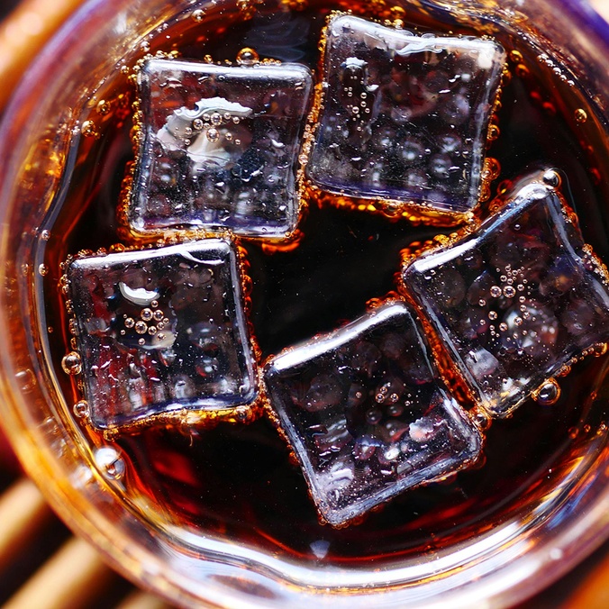 A dark-coloured soft drink in a glass with ice