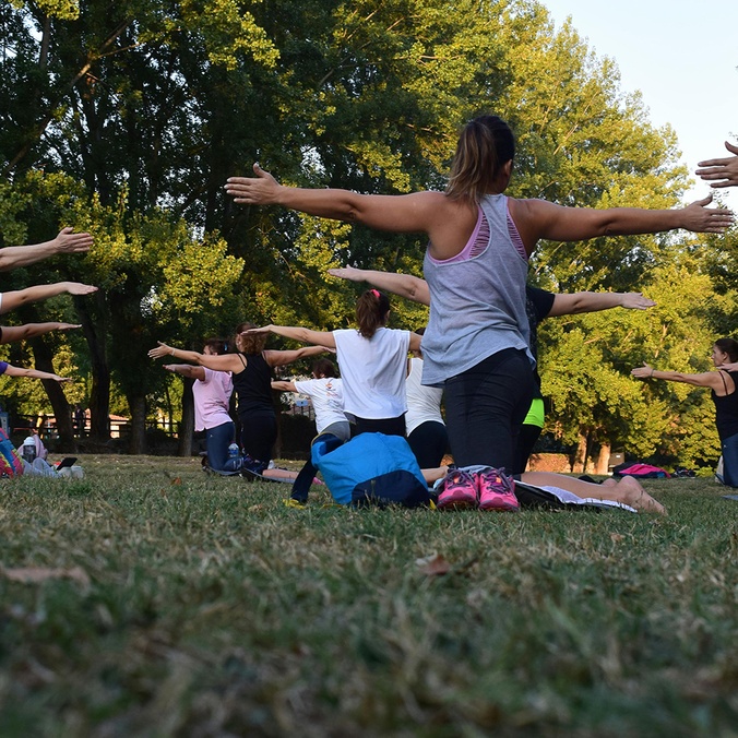 Women performing yoga on green grass near trees
