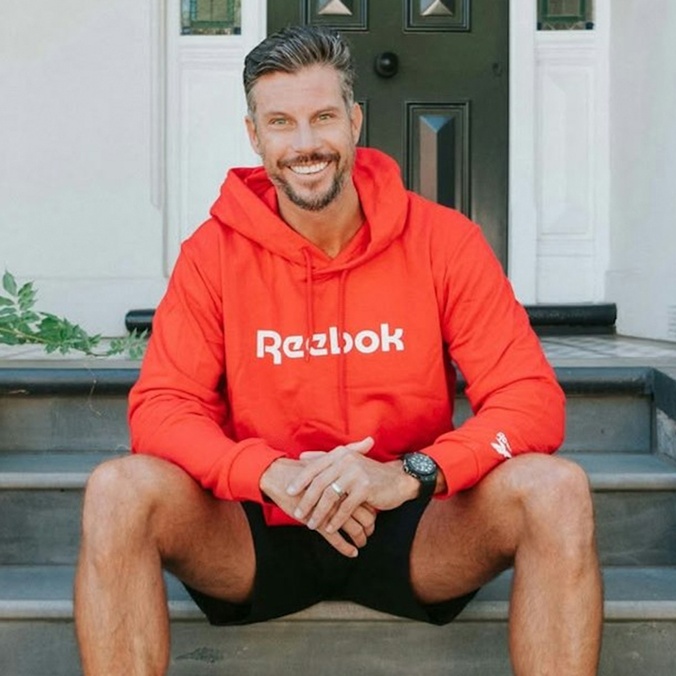 A man with a beard sitting on a set of stairs wearing a red hoodie