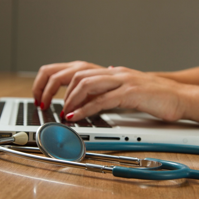 student typing on laptop with stethoscope on side