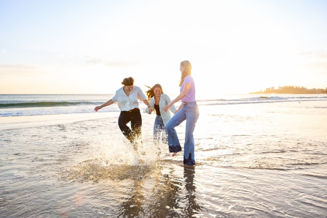 Three students in casual clothes run around on the beach.