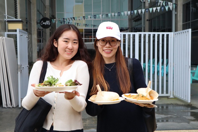 Two students holding up plates of food, smiling