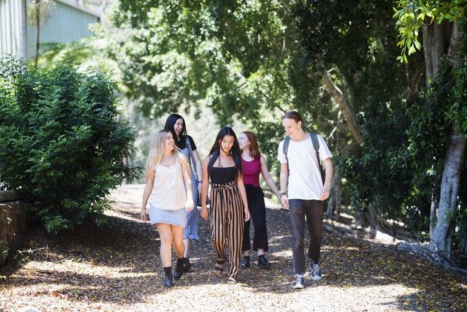 Young group of students walking through a leafy green path talking and smiling