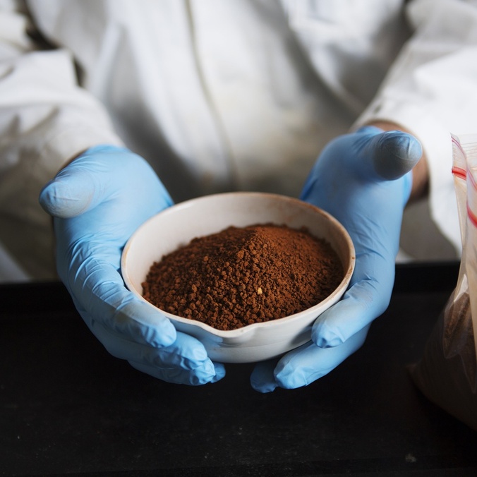 blue gloves holding bowl of red mud