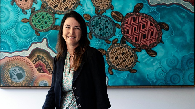 Kylie Day - Doctorate of Indigenous Philosophies (DIP) sitting in front of Indigenous artwork